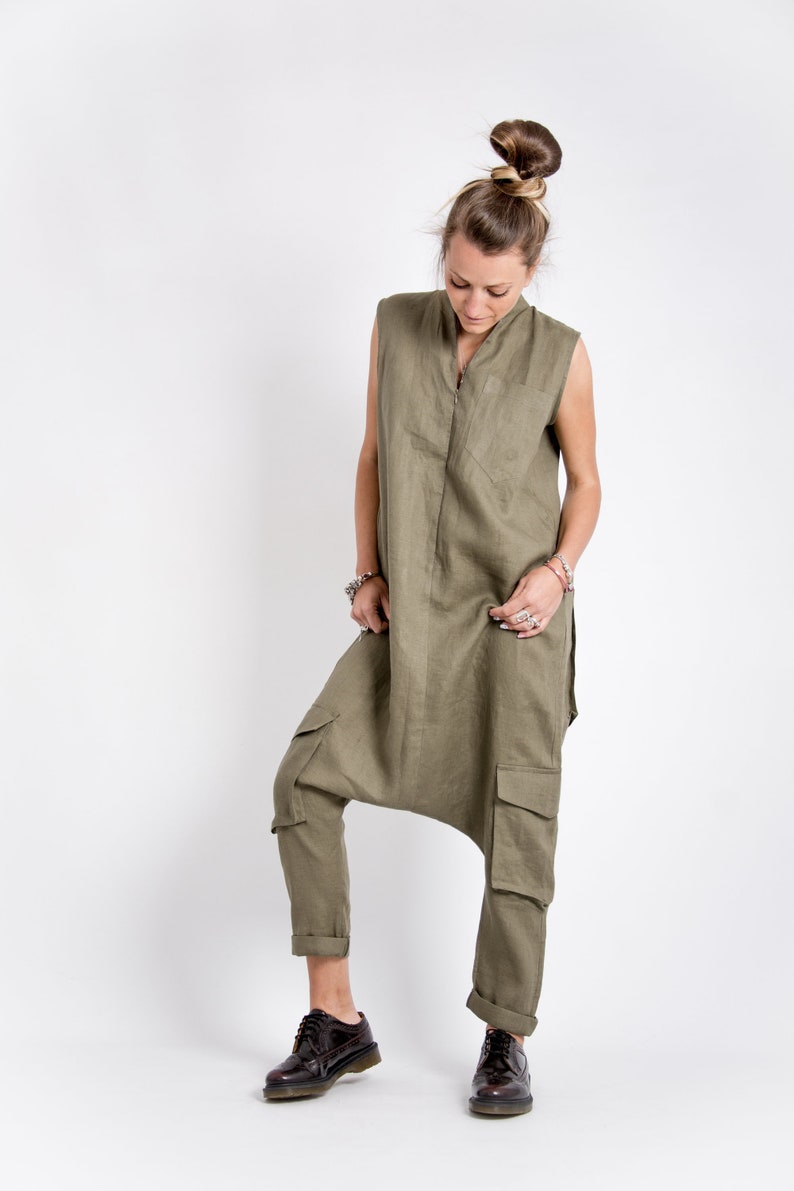 May include: A woman wearing a green linen jumpsuit with a zipper down the front and cargo pockets. She is wearing brown leather shoes.