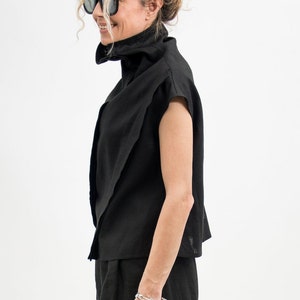 May include: A woman wearing a black mock neck shirt with a short sleeve and black pants. She is wearing a silver bracelet and rings on her fingers.