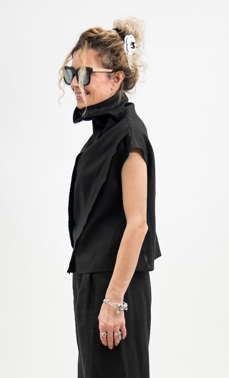 May include: A woman wearing a black mock neck shirt with a short sleeve and black pants. She is wearing a silver bracelet and rings on her fingers.