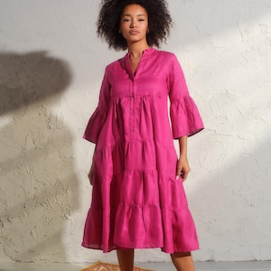 May include: A pink tiered linen dress with a button-up front and 3/4 sleeves. The dress has a relaxed fit and a midi length.