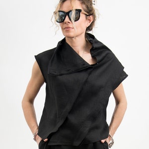 May include: A black linen top with a draped collar and short sleeves. The top is worn with black linen pants.