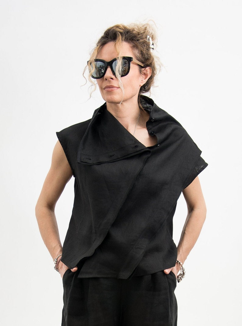 May include: A black linen top with a draped collar and short sleeves. The top is worn with black linen pants.