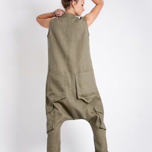 May include: A khaki linen jumpsuit with large cargo pockets and a loose fit. The jumpsuit has a sleeveless design and a relaxed, comfortable look.