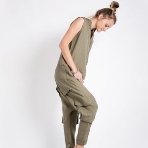 May include: A woman wearing a green linen jumpsuit with a loose fit and a sleeveless design. She is wearing brown leather shoes with laces.