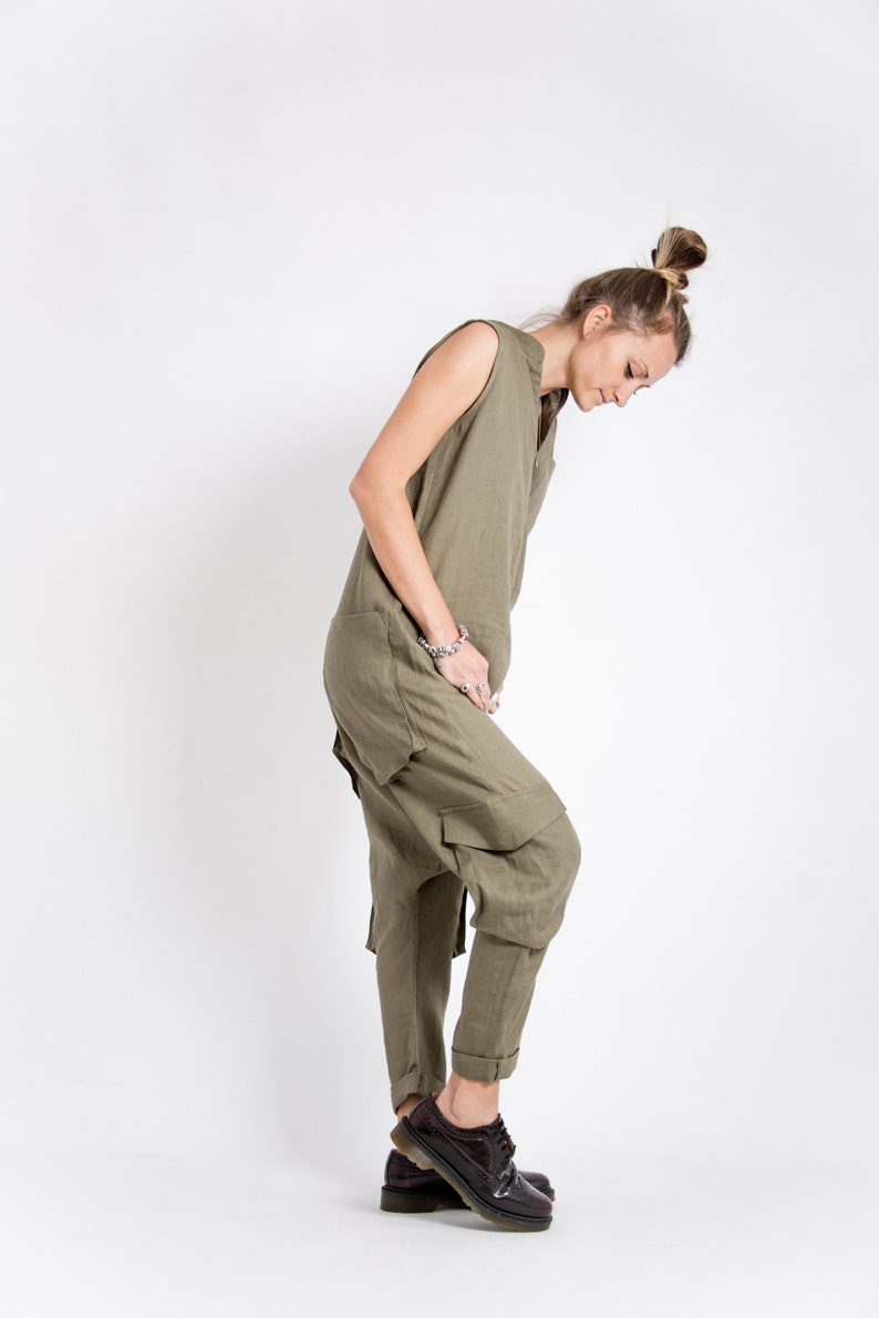 May include: A woman wearing a green linen jumpsuit with a loose fit and a sleeveless design. She is wearing brown leather shoes with laces.