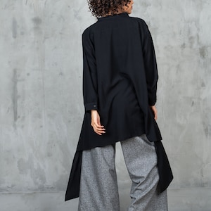 May include: A black long-sleeved shirt with a high collar and a long, asymmetrical hemline. The shirt is worn over gray wide-leg pants.