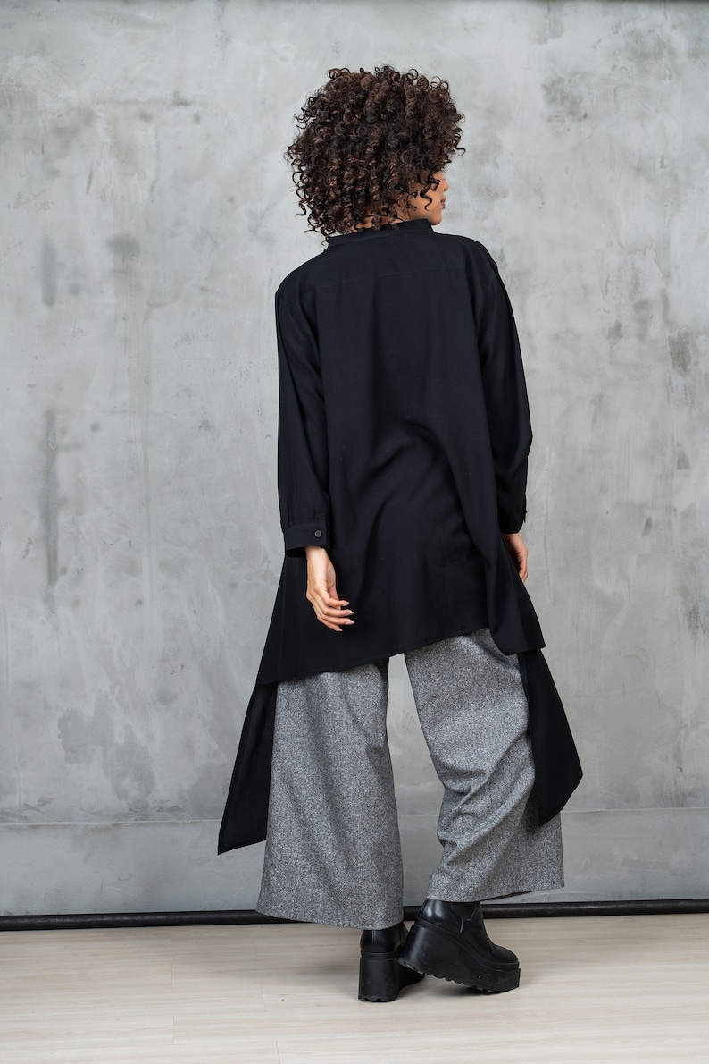 May include: A black long-sleeved shirt with a high collar and a long, asymmetrical hemline. The shirt is worn over gray wide-leg pants.