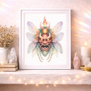 May include: A framed watercolor print featuring a fantastical creature with a red demon mask face, insect wings, and floral accents. The artwork is set against a soft, neutral background, with a white frame. The print is displayed on a shelf with decorative items.