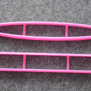 Pode incluir: Duas ferramentas de decoração de bolos de plástico rosa. A ferramenta superior tem forma oval com três recortes. A ferramenta inferior é retangular com três recortes.