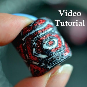Könnte beinhalten: Nahaufnahme eines zylindrischen Objekts mit einem Wirbelmuster aus Rot, Schwarz und Weiß. Das Objekt wird zwischen den Fingern gehalten. Die Worte "Video Tutorial" sind in weißem Text.