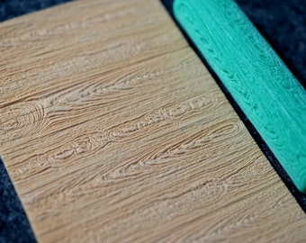 May include: A green rolling pin with a wood grain pattern, used for creating wood grain texture on fondant or other edible materials.