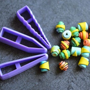 May include: A collection of colorful polymer clay beads and three purple clay cutters. The beads are cylindrical with yellow, green, orange, and blue accents. The cutters are in various shapes, including a wavy edge.