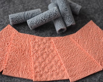 May include: Five silicone rolling pins with different embossed patterns, and five matching silicone mats with the same patterns. The rolling pins are gray and the mats are peach.