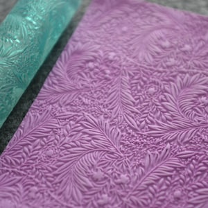 May include: A teal blue rolling pin with a floral design and a purple silicone mat with a matching floral design.