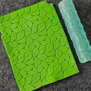 Könnte beinhalten: Ein grüner Silikon-Nudelholz mit einem Blatt-Muster und eine passende grüne Silikon-Matte mit einem Blatt-Muster.