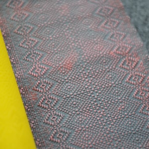 Può includere: Un rullo giallo con una superficie testurizzata è accanto a un pezzo di tessuto con un motivo geometrico rosa e grigio.