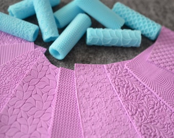May include: A set of 10 silicone rolling pins and 8 silicone mats for baking and decorating. The rolling pins are light blue and have various embossed patterns. The mats are lavender and have a variety of embossed patterns.