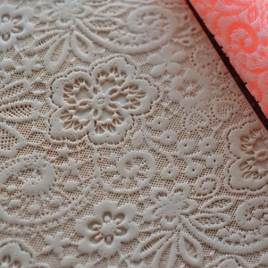 May include: A beige, textured rolling pin and a matching embossed surface, both featuring a delicate floral lace pattern. The rolling pin is a vibrant coral color, and the design is ideal for baking and crafting.