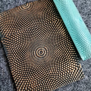 May include: A close-up of a textured, brown and black patterned leather stamp with a light blue rolling tool. The stamp has a circular pattern with a smaller circle in the centre.