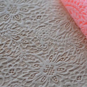 May include: A close-up of a white silicone rolling pin with a delicate floral pattern. The rolling pin is designed for creating embossed designs on fondant or other edible materials.