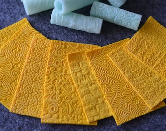 May include: Eight yellow textured silicone mats with different embossed patterns. The mats are arranged in a fan shape on a gray surface.