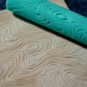 Pode incluir: Um rolo de pastelaria verde-azulado com um padrão ondulado. O rolo é usado para criar um padrão texturizado em uma superfície.