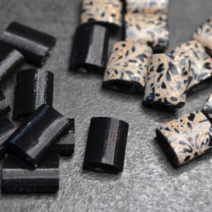 May include: A collection of black and white ceramic beads with a floral pattern. The beads are rectangular and have a glossy finish.