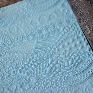 Può includere: Un mattarello blu con una varietà di motivi intricati in rilievo sulla superficie. Il mattarello viene utilizzato per creare motivi decorativi in ​​argilla, fondant o pasta.