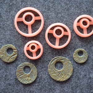 May include: A set of six round, decorative clay pieces. Four of the pieces are pink and have a raised, circular design. Two of the pieces are gold and have a textured, swirling design.