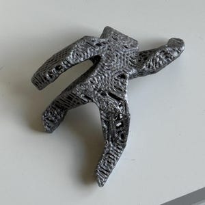 May include: A grey, 3D-printed sculpture of a person in a star shape, with arms and legs outstretched. The sculpture has a textured surface and is placed on a white surface.
