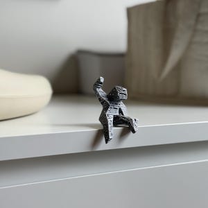 May include: A small, abstract sculpture of a person sitting on a ledge. The figure is black and white with a geometric pattern. The sculpture is perched on the edge of a white surface.