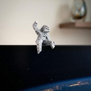 May include: A silver-coloured, geometric sculpture of a person sitting on the edge of a dark screen. The sculpture has a detailed, open design. The screen displays a view of Earth from space, with city lights visible.
