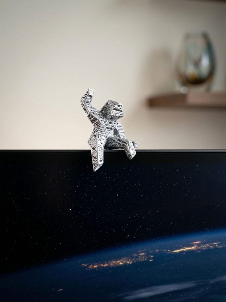 May include: A silver-coloured, geometric sculpture of a person sitting on the edge of a dark screen. The sculpture has a detailed, open design. The screen displays a view of Earth from space, with city lights visible.