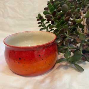 May include: A small, orange ceramic bowl with black speckles. The bowl has a white interior and a gradient of orange shades.