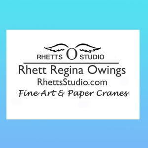 Op de afbeelding: Een witte rechthoekige afbeelding op een lichtblauwe achtergrond met de tekst "RHETTS STUDIO" boven "Rhett Regina Owings" en "RhettsStudio.com". Daaronder staat de tekst "Fine Art & Paper Cranes".