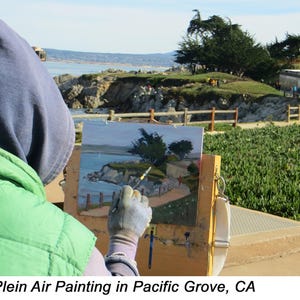 Op de afbeelding: Een kunstenaar schildert een kustlandschap in de open lucht. Het schilderij toont een kustlijn met bomen, een pad en gebouwen. De kunstenaar draagt een groen vest en een blauwe hoodie. De tekst "Plein Air Painting in Pacific Grove, CA" staat onderaan.