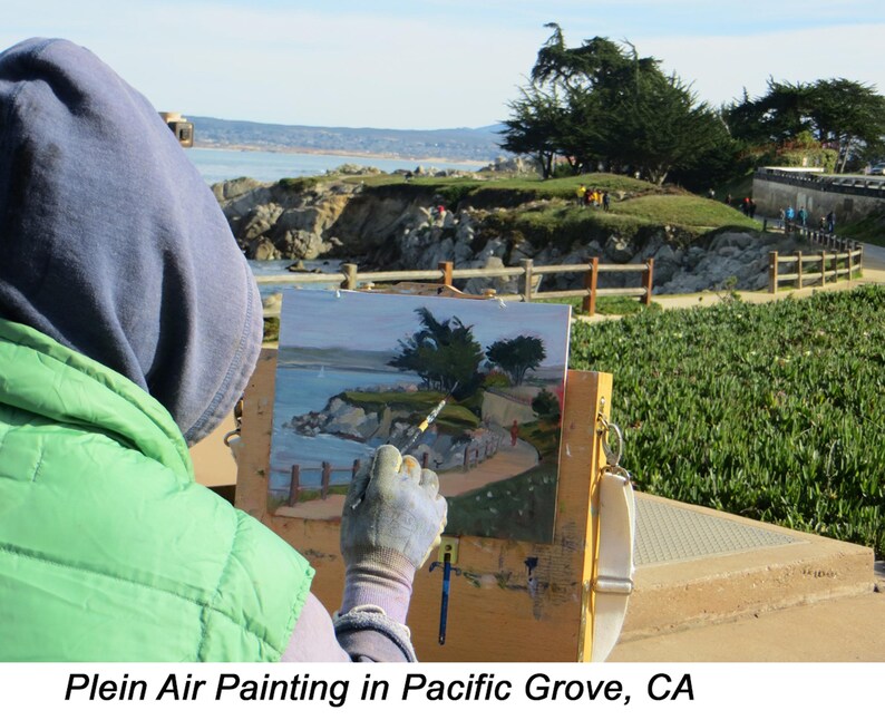 Op de afbeelding: Een kunstenaar schildert een kustlandschap in de open lucht. Het schilderij toont een kustlijn met bomen, een pad en gebouwen. De kunstenaar draagt een groen vest en een blauwe hoodie. De tekst "Plein Air Painting in Pacific Grove, CA" staat onderaan.