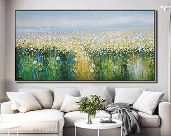 May include: A large abstract painting of a field of white flowers with green and yellow accents. The painting is framed in a thin gold frame and is hanging on a white wall above a white couch.