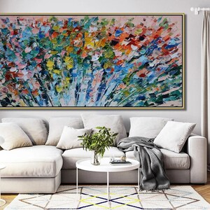 May include: Abstract painting with a colorful, textured, brushstroke style. The painting features a variety of colors, including blue, green, yellow, orange, and pink. The painting is framed in a gold frame and is hanging on a wall in a living room setting.