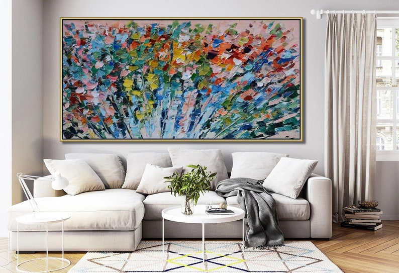 May include: Abstract painting with a colorful, textured, brushstroke style. The painting features a variety of colors, including blue, green, yellow, orange, and pink. The painting is framed in a gold frame and is hanging on a wall in a living room setting.