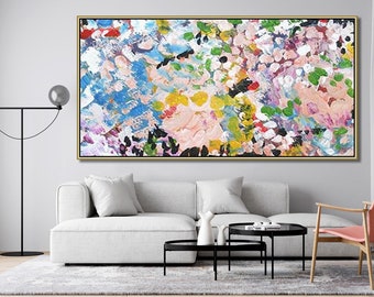 May include: Abstract floral painting in a gold frame. The artwork features a vibrant mix of colors, including blue, pink, yellow, and green, applied with thick brushstrokes. The painting is displayed above a white sofa in a modern living room setting.