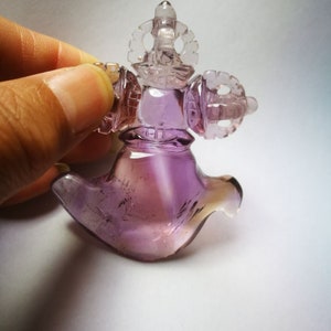 May include: A purple amethyst crystal carved into a detailed, intricate design. The crystal is shaped like a bird with a crown on its head.