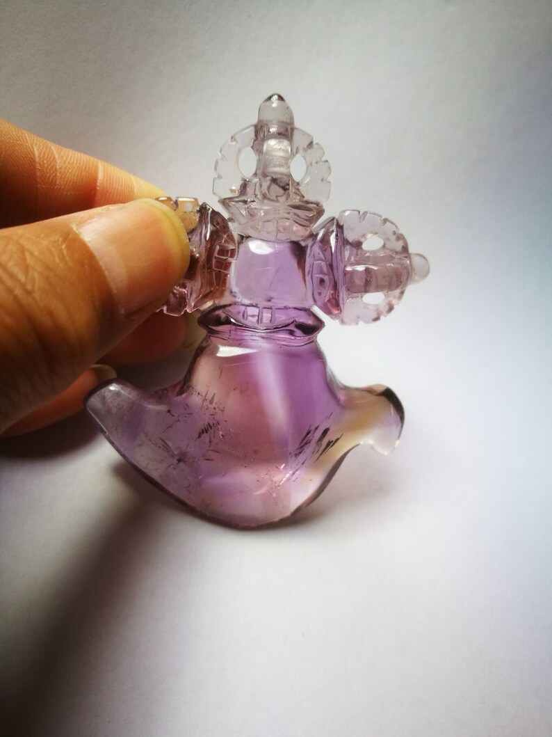 May include: A purple amethyst crystal carved into a detailed, intricate design. The crystal is shaped like a bird with a crown on its head.