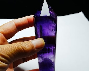 May include: A deep purple amethyst crystal point with a clear tip. The crystal is faceted and has a smooth, polished finish.