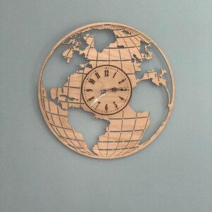 May include: A wooden clock shaped like a globe with a brown wood grain finish. The clock face is white with black numbers and hands. The globe features a detailed outline of the continents.