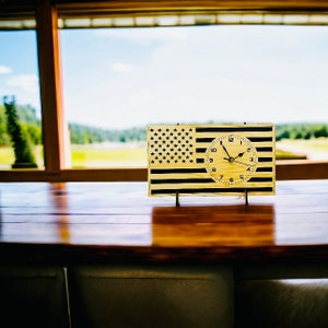 May include: A wooden clock with a black and white American flag design. The clock face is white with black numbers and hands.