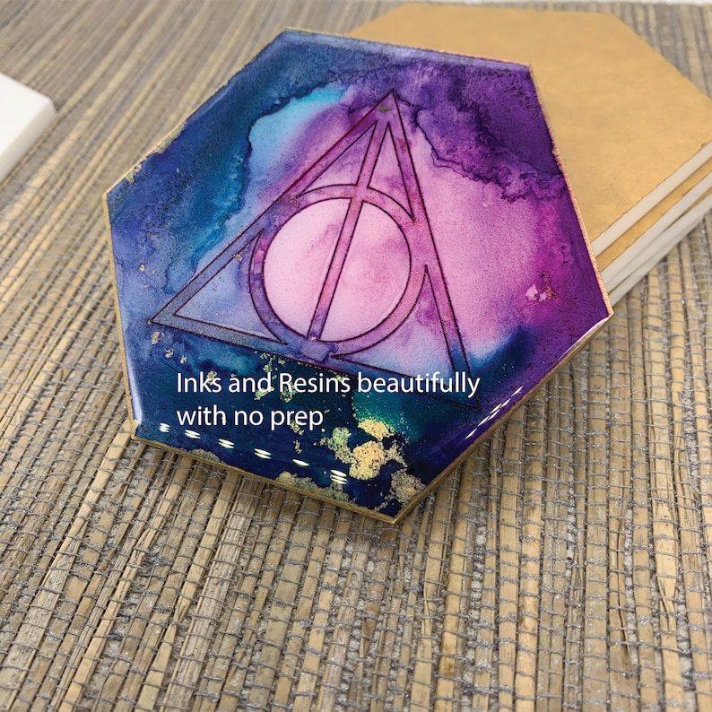 May include: Hexagon-shaped coaster with a colorful ink and resin design. The coaster features a purple, blue, and pink watercolor effect with a gold accent. The Deathly Hallows symbol is in the center. Text on the coaster reads "Inks and Resins beautifully with no prep."