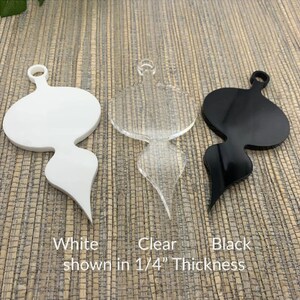 May include: Three acrylic ornaments in white, clear, and black. Each ornament has a rounded top with a hole for hanging and a stylized, elongated bottom. The text at the bottom reads "White, Clear, Black shown in 1/4" Thickness."