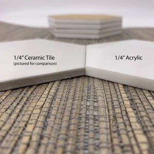 May include: Close-up comparison of two white hexagonal tiles. One is labeled "1/4" Ceramic Tile" and the other "1/4" Acrylic." The ceramic tile has a gray edge, while the acrylic tile has a clean white edge. A stack of similar tiles is in the background.