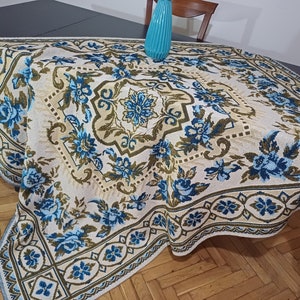 May include: A white tablecloth with a blue and green floral pattern. The tablecloth has a square shape and is made of a soft, textured fabric.